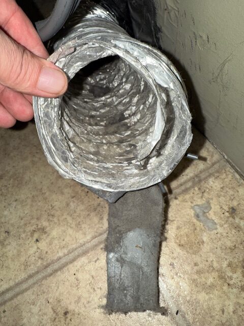 A hand holds a flexible duct, showing dust buildup