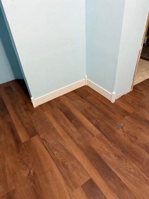 Brown laminate flooring meets a light blue wall in a corner, showcasing freshly installed baseboards