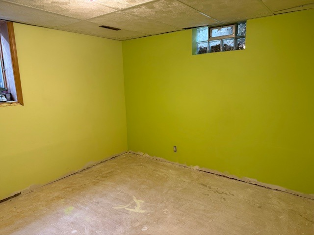 Bright lime green walls in an unfinished basement room with bare concrete flooring and a small glass block window.
