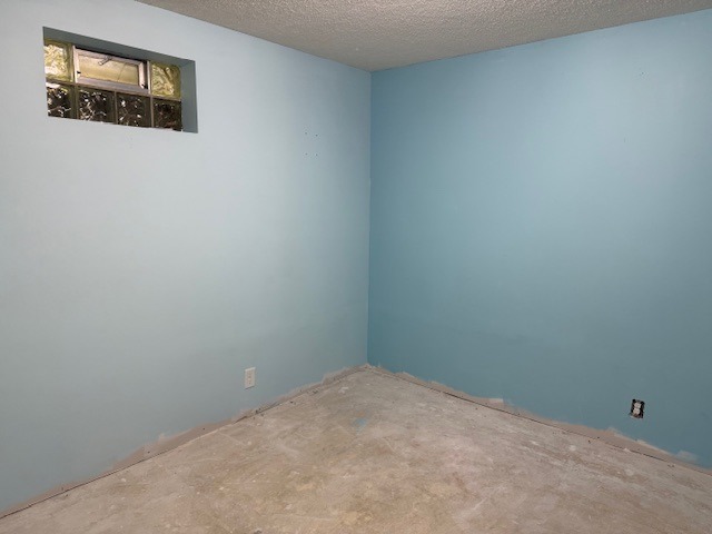 Empty room with freshly painted light blue walls and unfinished floor. A small window allows natural light, suggesting a renovation project.