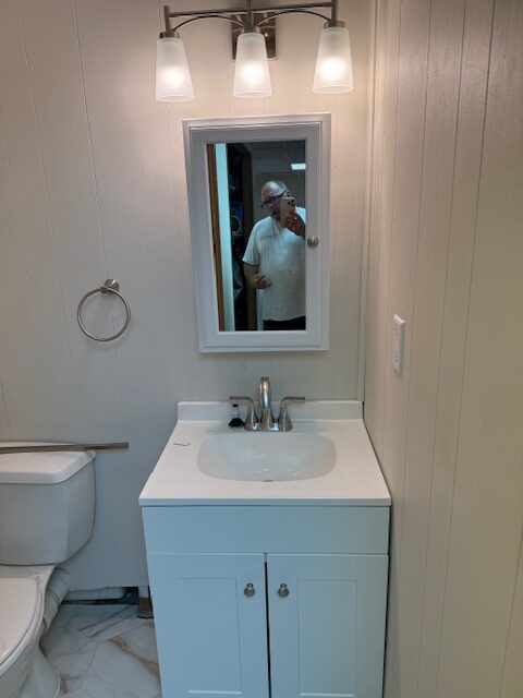 Modern bathroom featuring a white vanity with a sink, a mirror, and three light fixtures. A toilet is visible on the left, creating a clean and functional space.