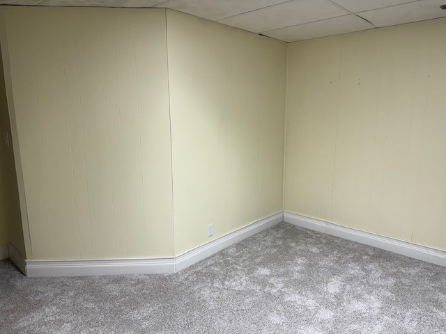Empty corner of a room with yellow walls and soft gray carpet, highlighting a clean, well-lit space suitable for various uses.