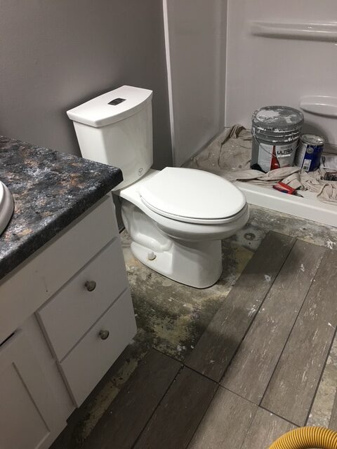 Newly renovated bathroom with a white toilet and sink on a tiled floor. Paint supplies and tools indicate ongoing remodeling work.